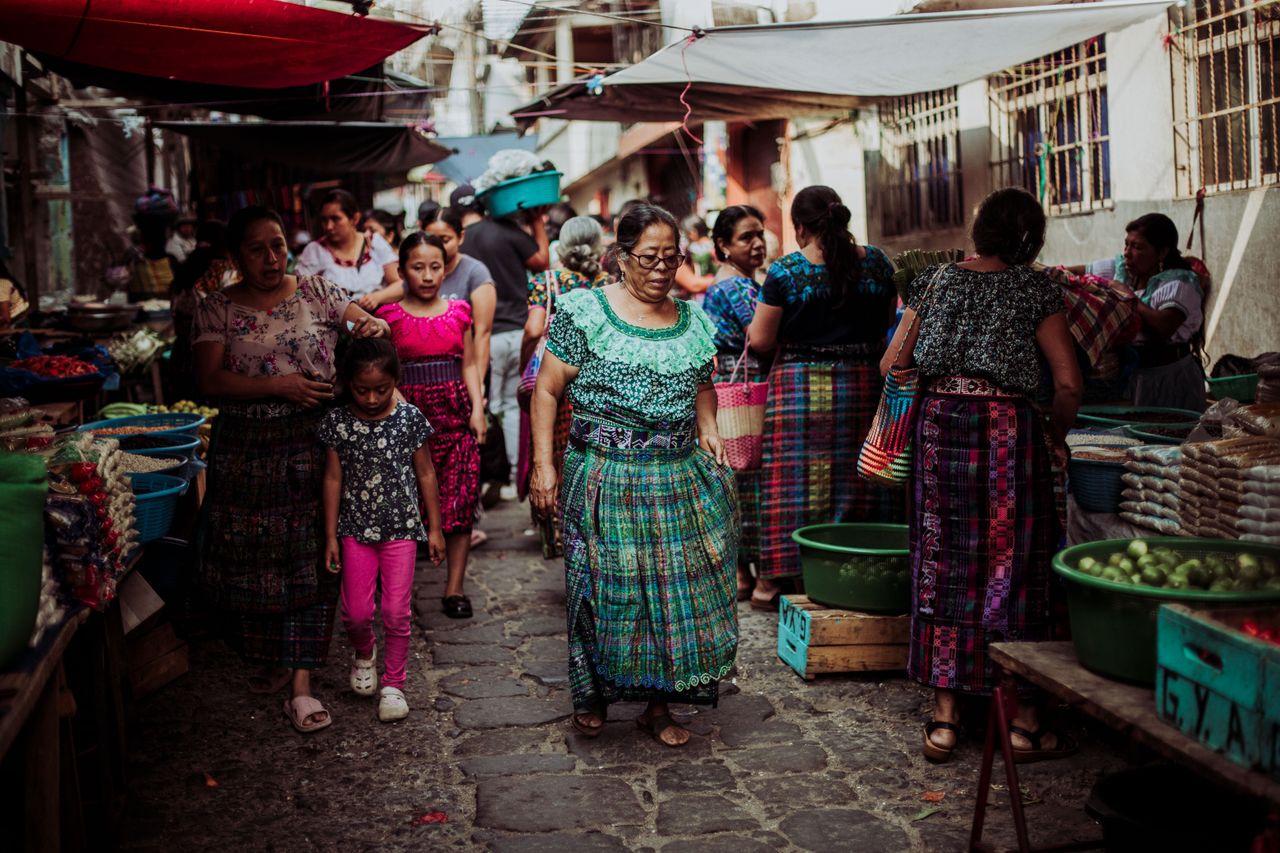Women and children in colorful traditional dresses at a bustling Guatemalan market.
