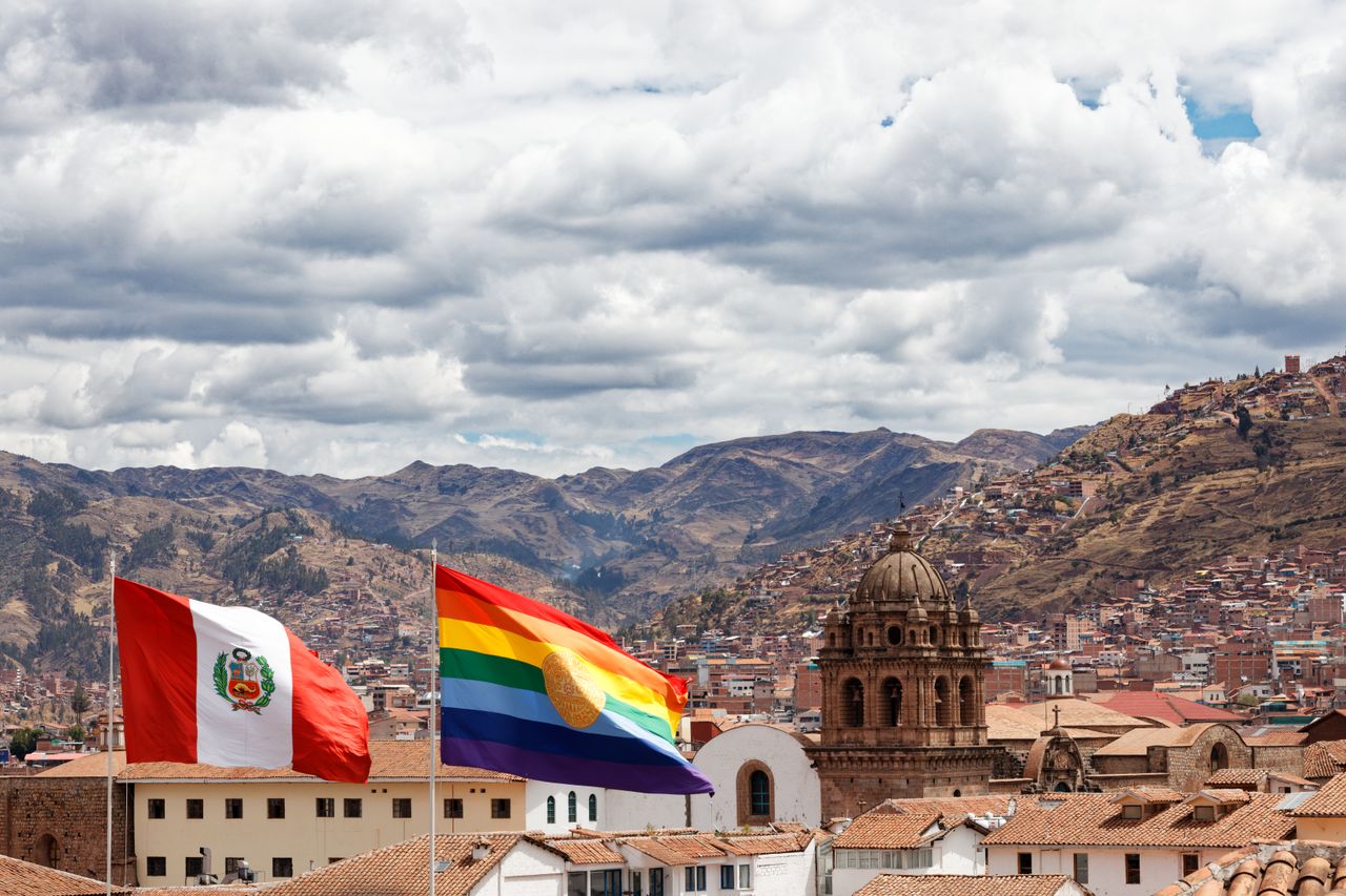 Cusco cityscape featuring Peruvian and Tahuantinsuyo flags against a mountain backdrop.